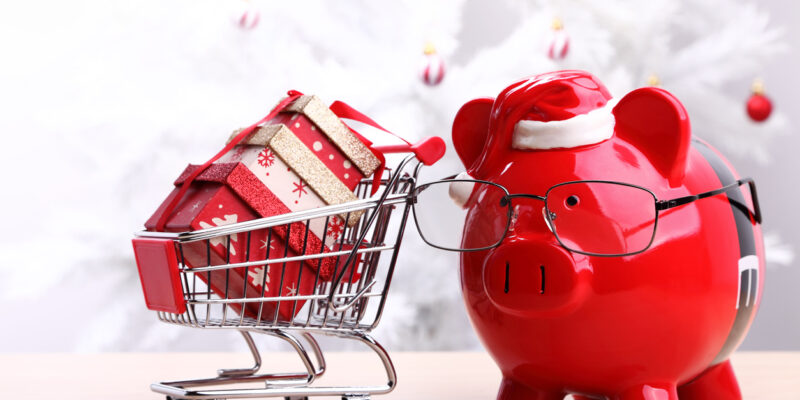 Piggy bank with glasses and a shopping cart in front of a white Christmas tree.
